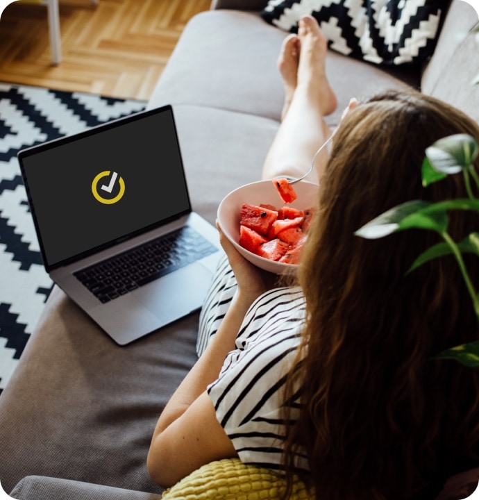 Kobieta jedząca owoc z leżącym obok laptopem z symbolem NortonLifeLock na ekranie.